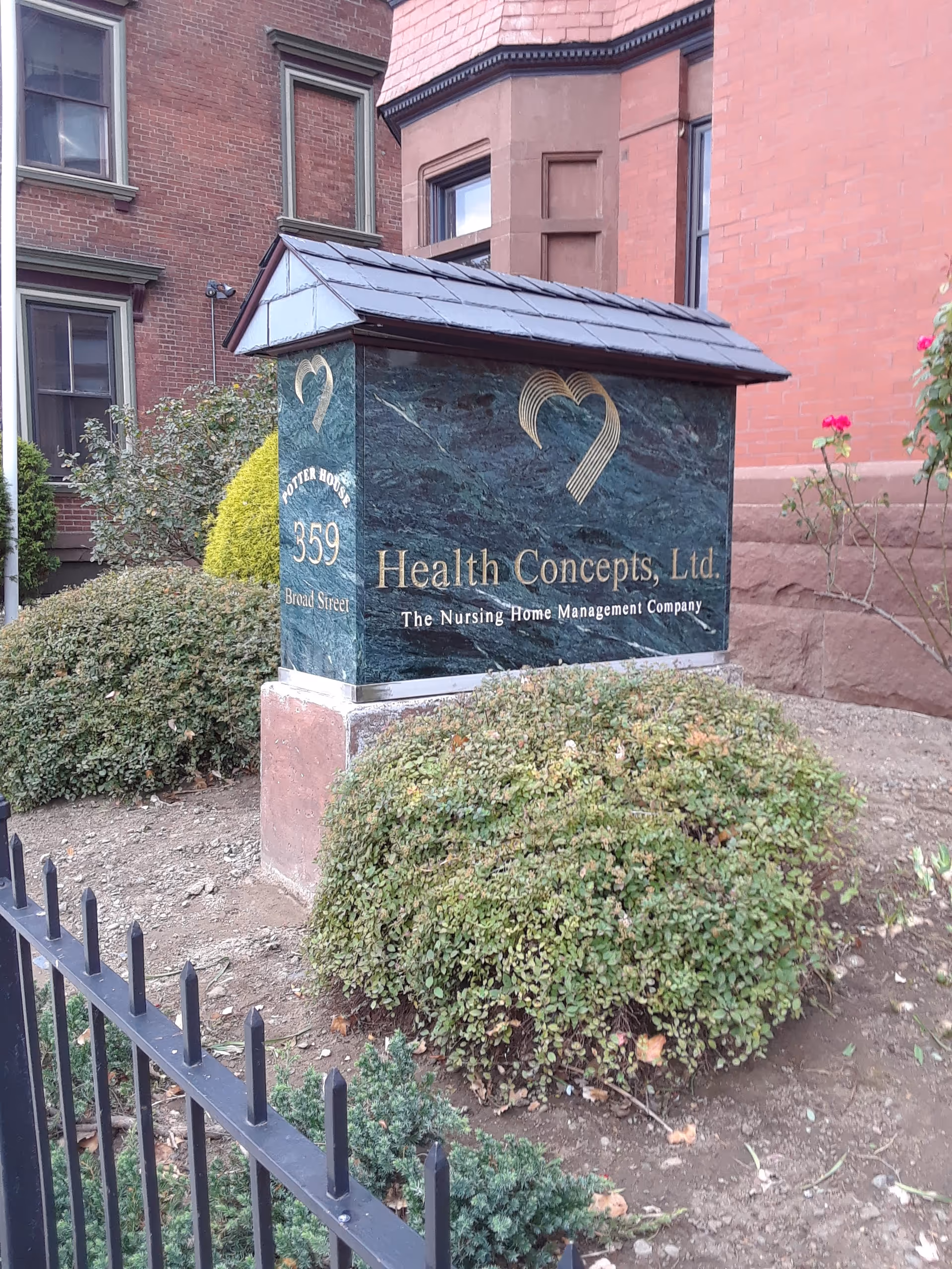 Exterior sign for Health Concepts, Ltd. nursing home, with shrubs and a brick building behind.