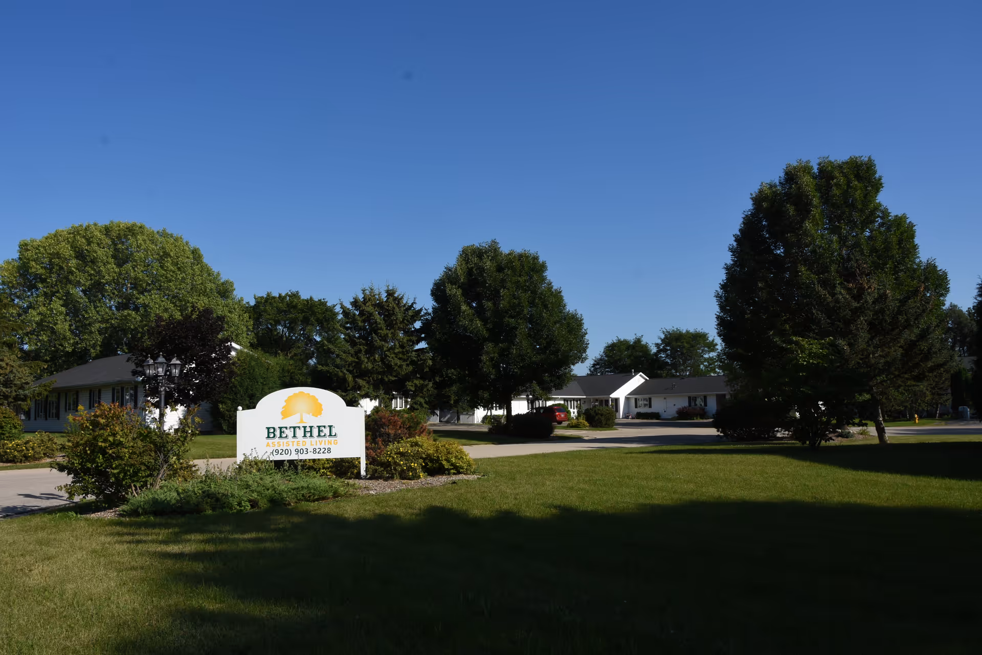 Wide view of Bethel Assisted Living exterior with manicured lawn and sign.