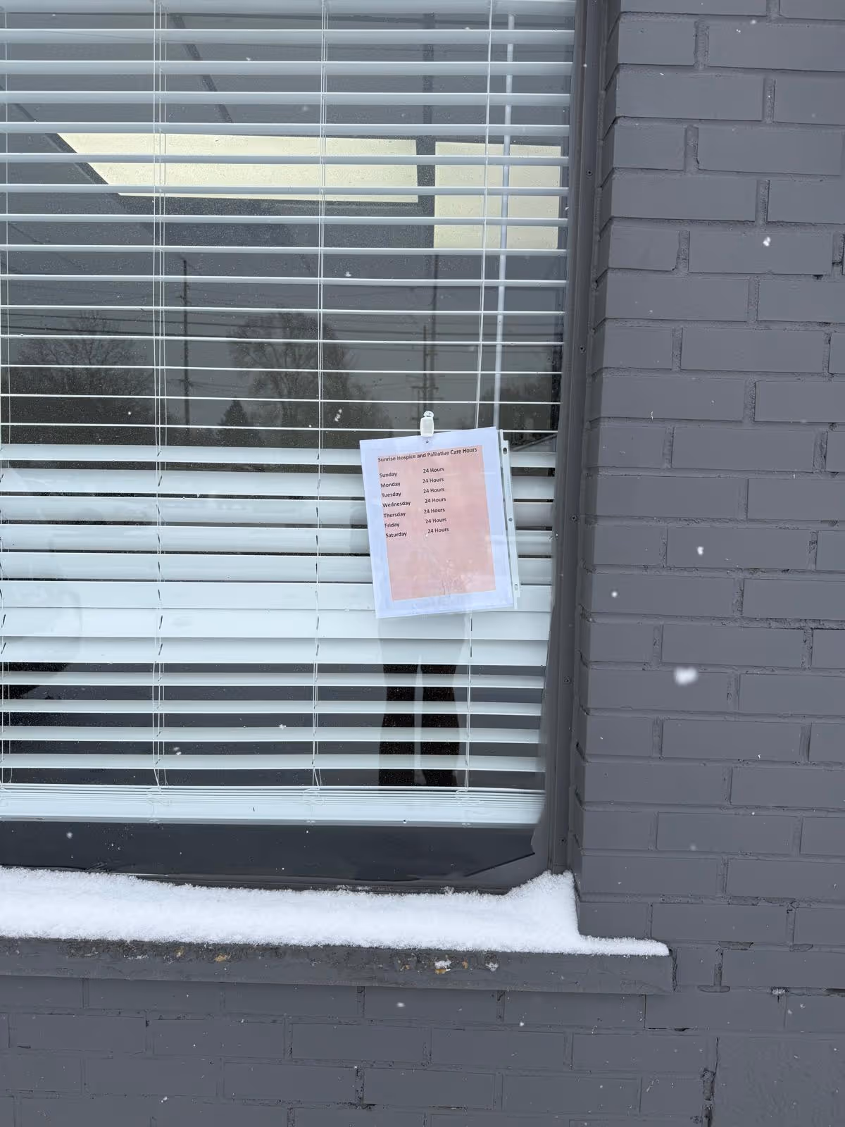 Snow on the windowsill beside a taped notice on a brick building