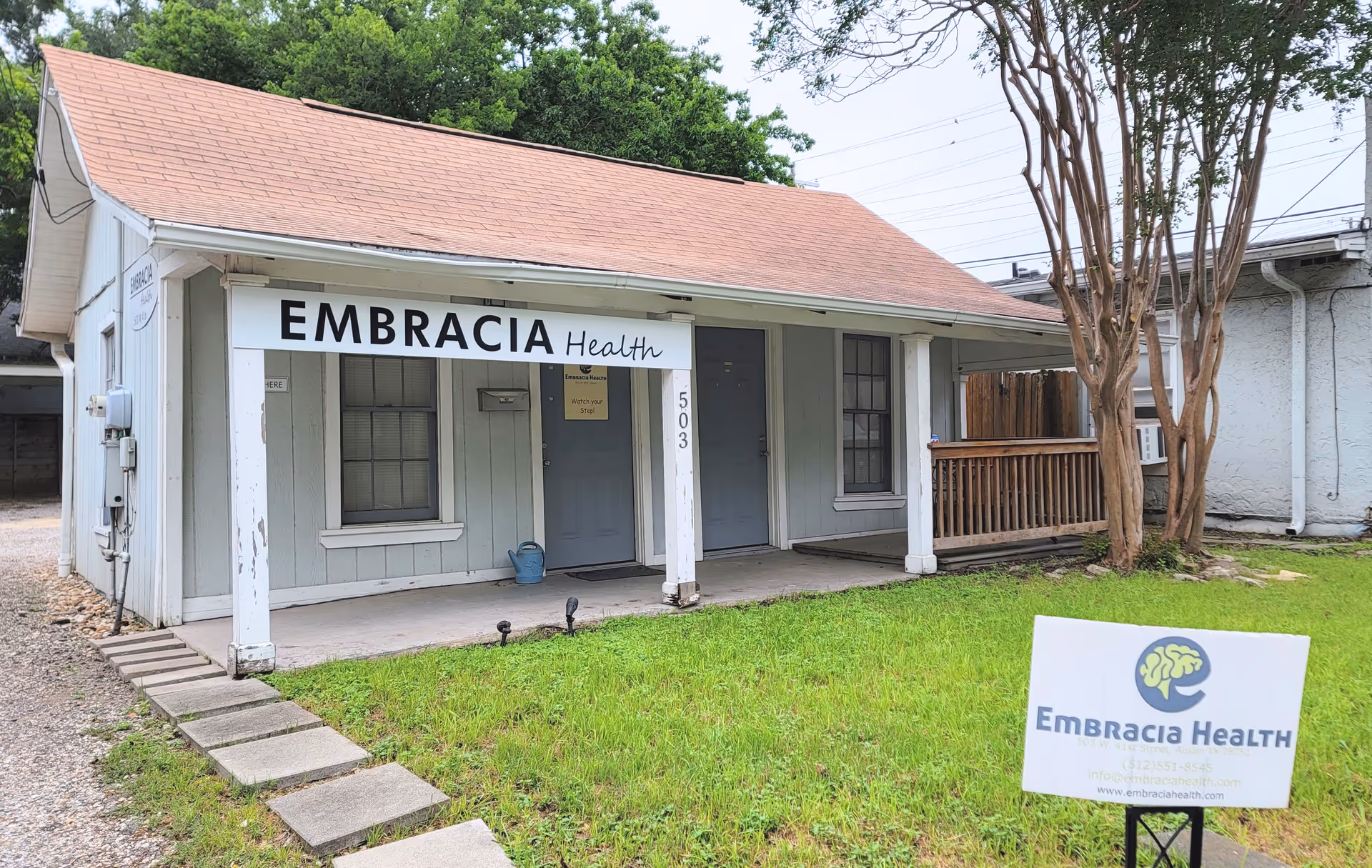 Exterior view of a small Embracia Health facility with front porch and sign.