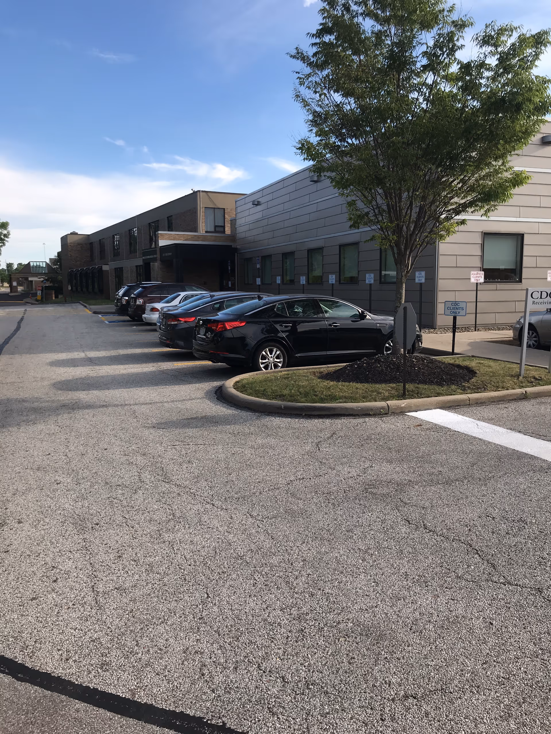 Parking lot in front of a modern senior living facility with cars and a tree