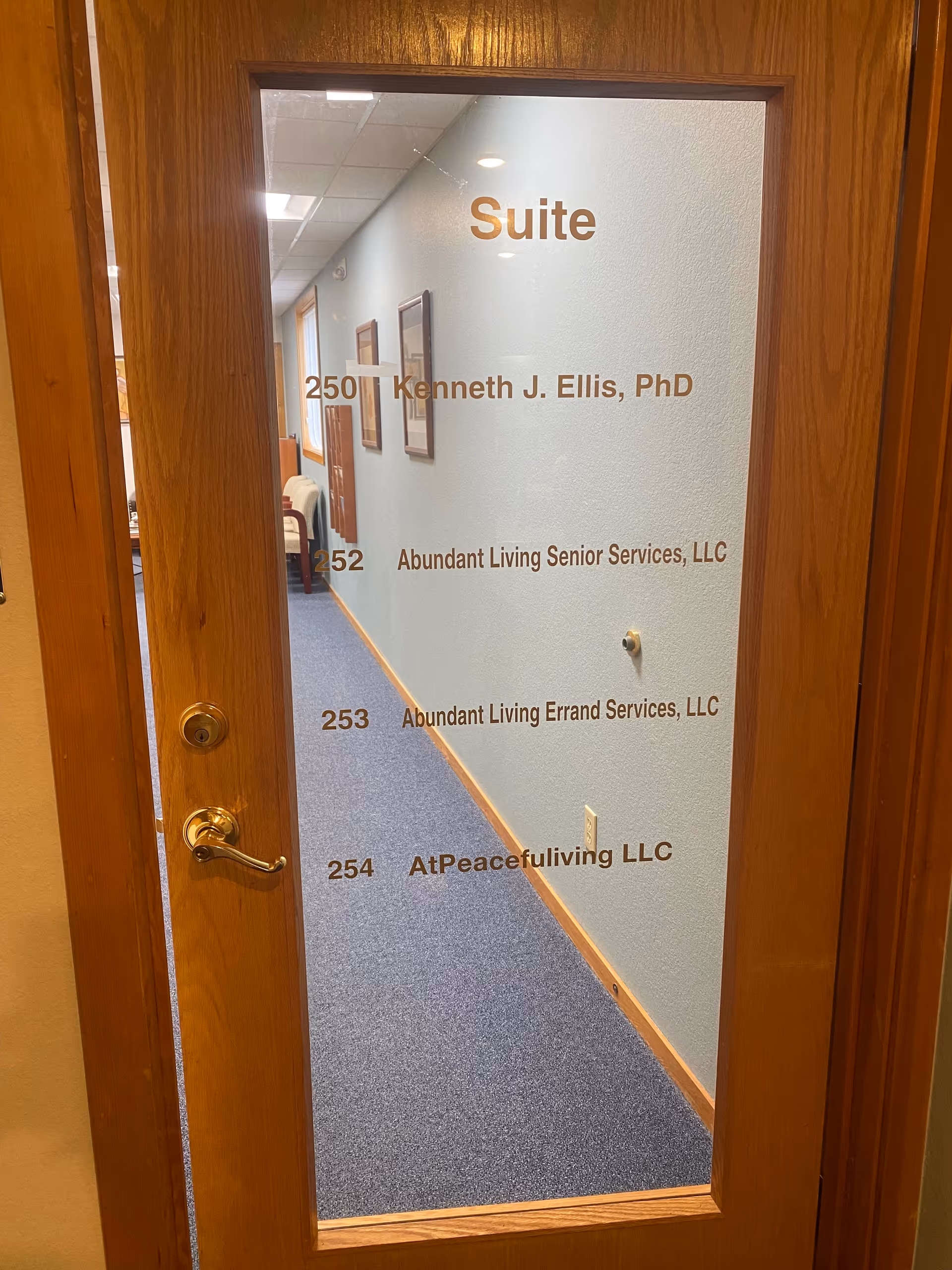 Glass-panel door showing Suite and room numbers along a blue-carpet hallway inside Abundant Living Senior Services