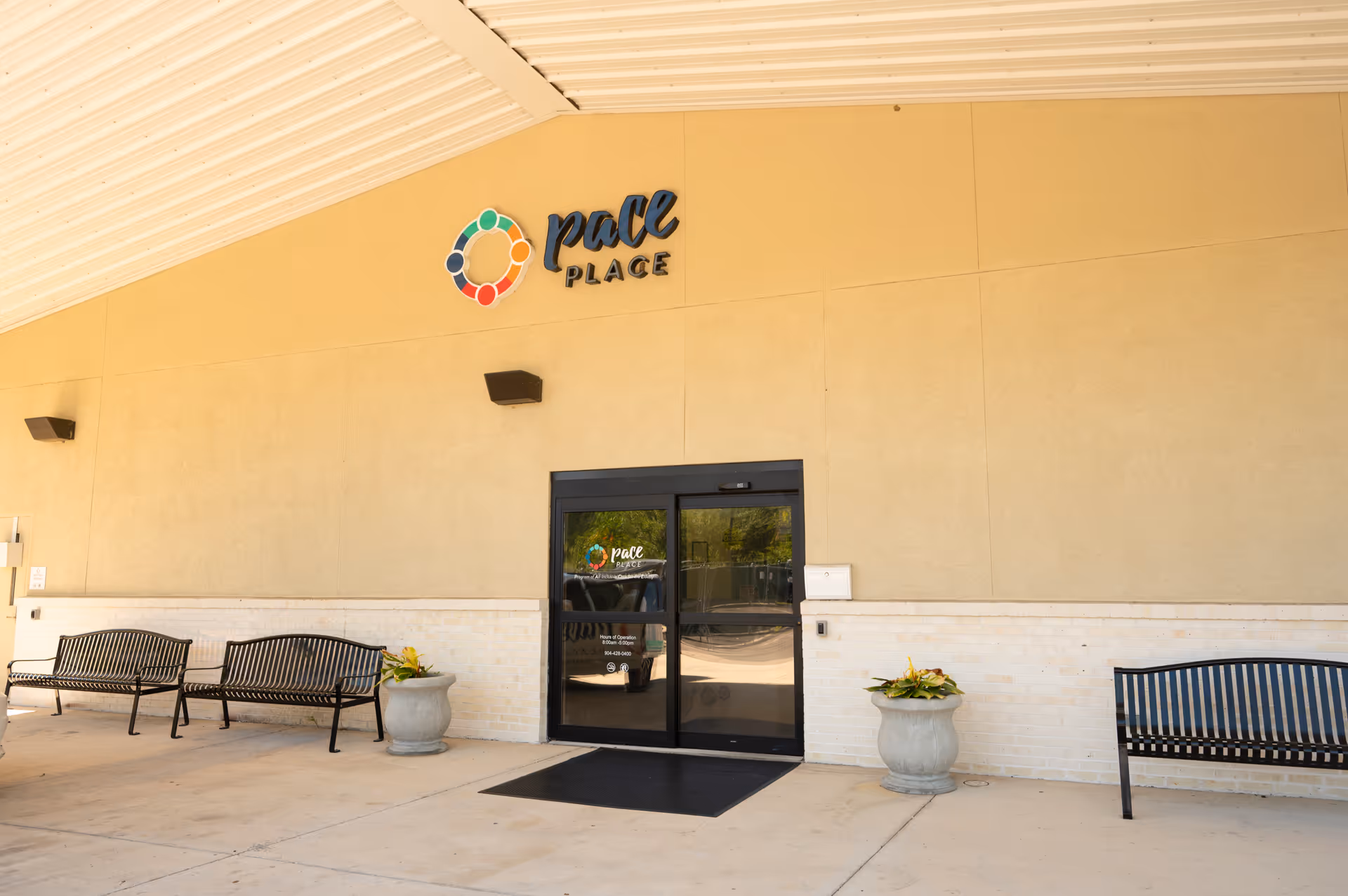 Exterior view of The PACE Place entrance with benches and potted plants.