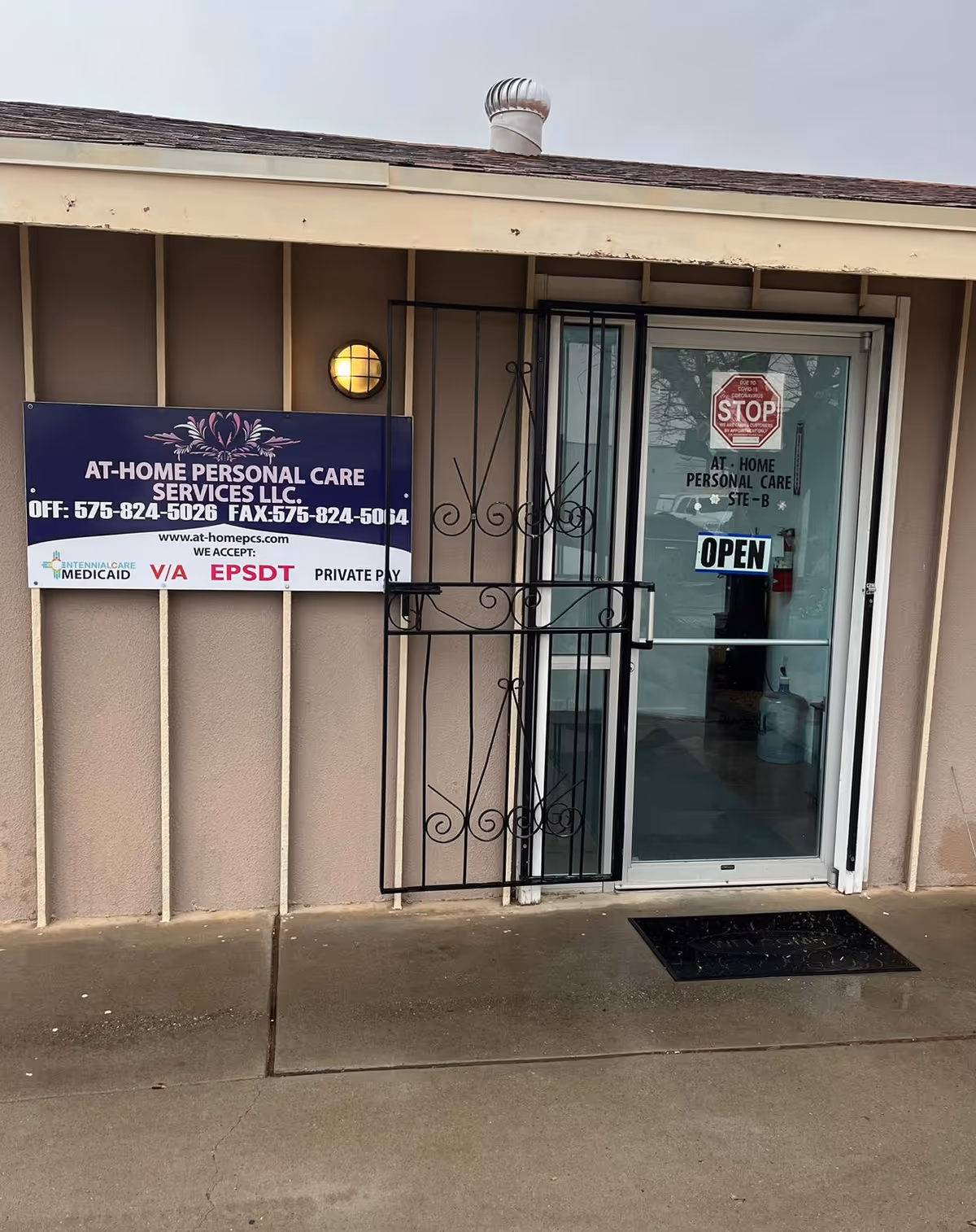 Exterior view of a facility entrance with a blue sign, metal gate, and OPEN sign.