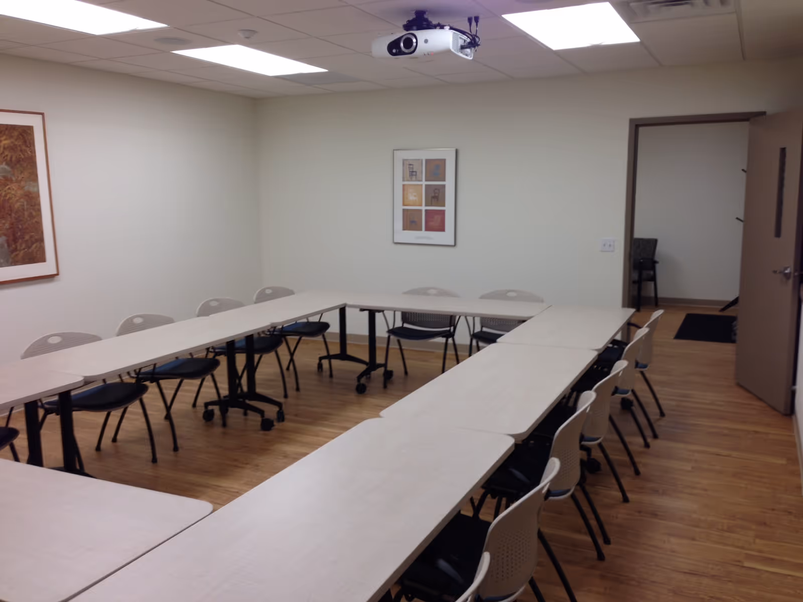 A conference-style classroom in a senior living facility with U-shaped desks and a ceiling projector.