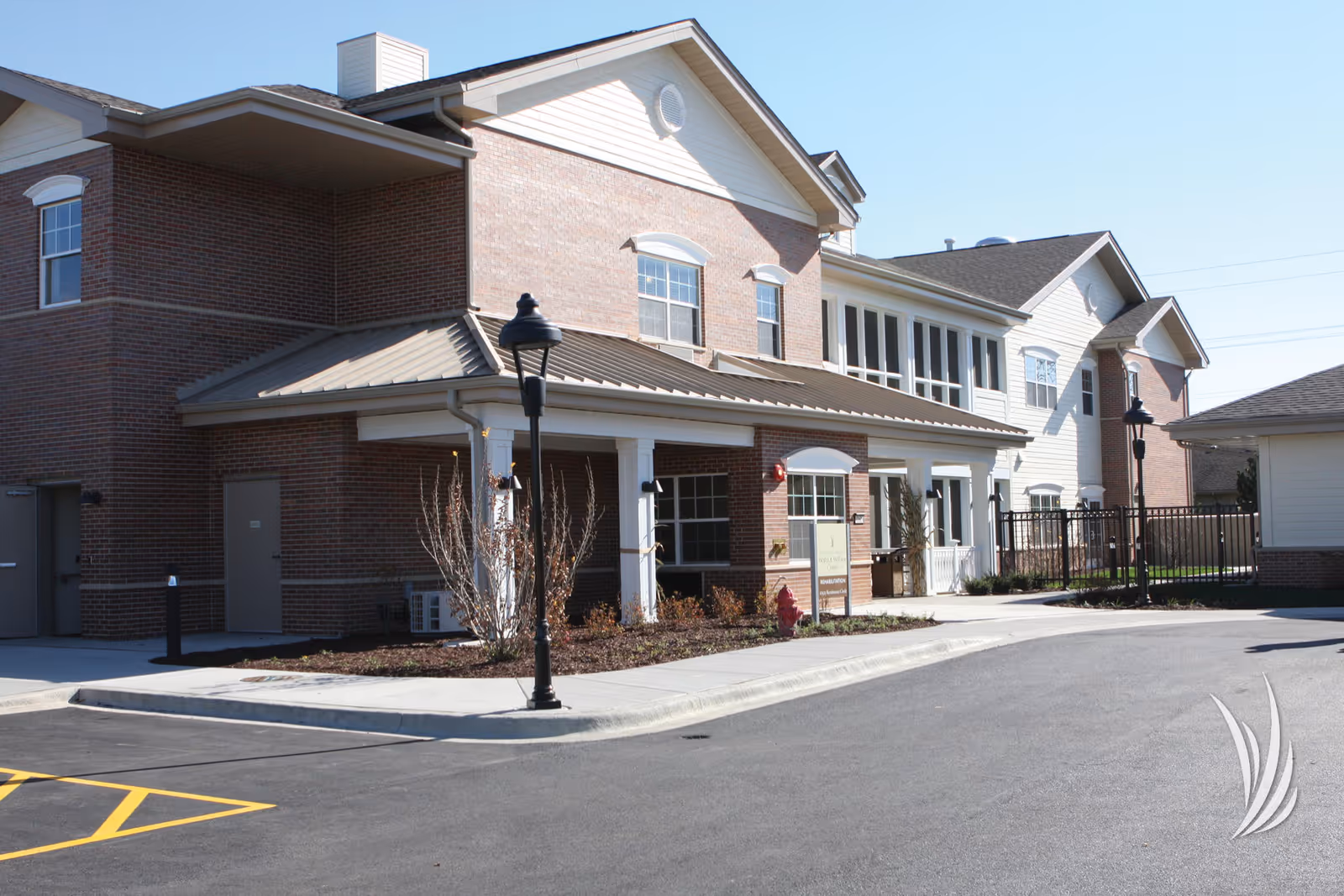 Brick and white siding senior living facility exterior with entrance and lampposts.