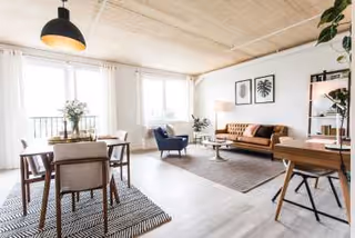 Bright living room with seating area, dining table, plants, and large windows.