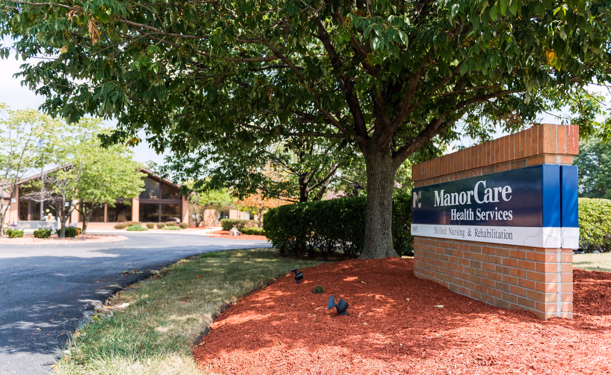 Front view of a senior care facility with a sign beside a tree.