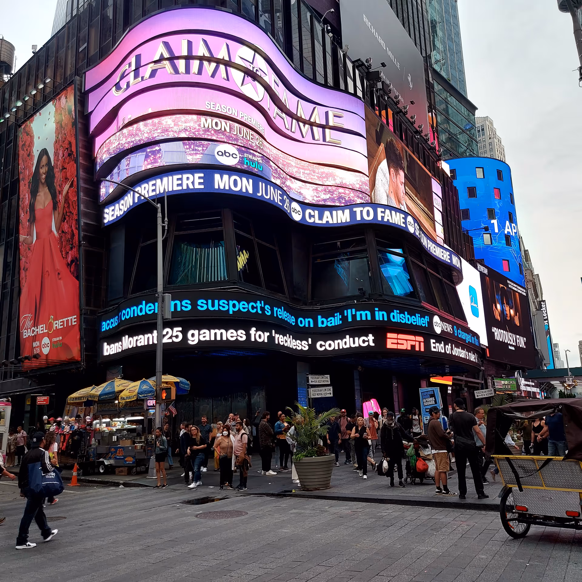 A bustling city building with large curved digital billboards and pedestrians outside.