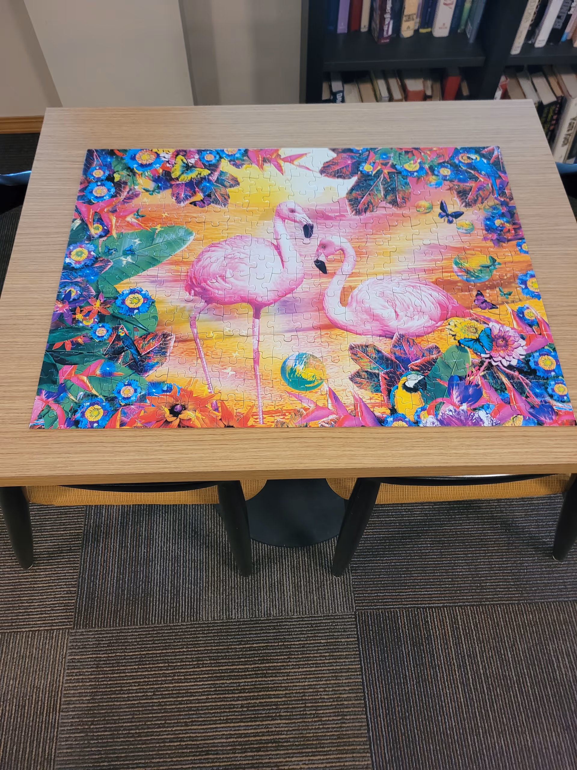 Colorful flamingo puzzle on a wooden table in a library-like common room.
