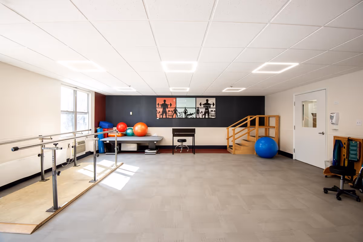 Well-lit rehabilitation room with parallel bars, exercise balls, and a small wooden staircase.
