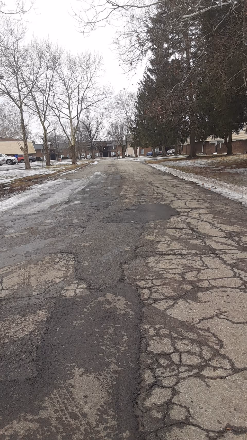 Cracked road leads to a distant brick senior living facility with bare trees.