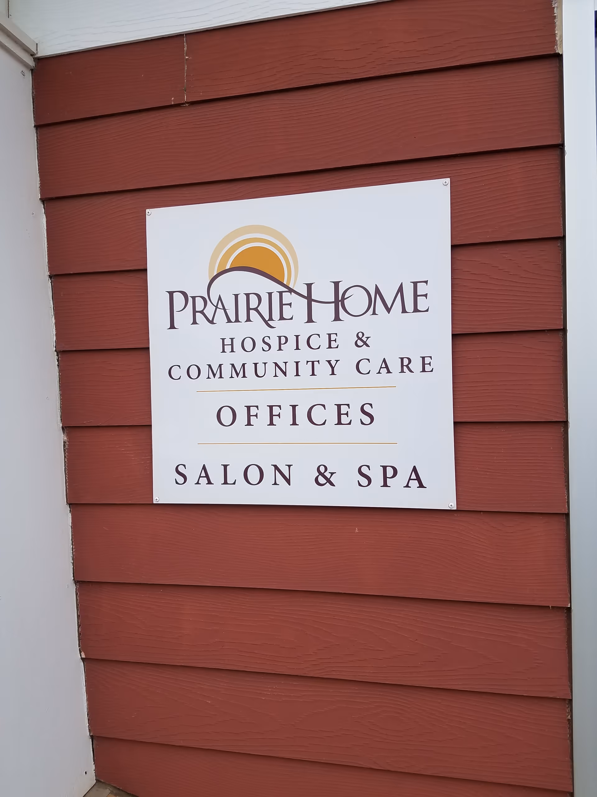 White sign reading Prairie Home Hospice & Community Care Offices, Salon & Spa on red siding.