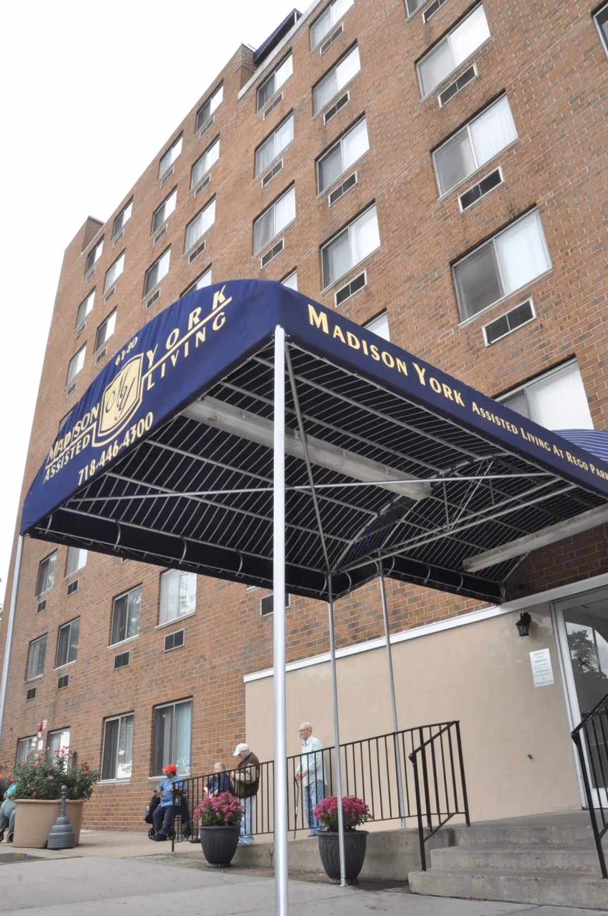Front entrance canopy reading "Madison York Assisted Living" on a multi-story brick building with a few people near the doorway.