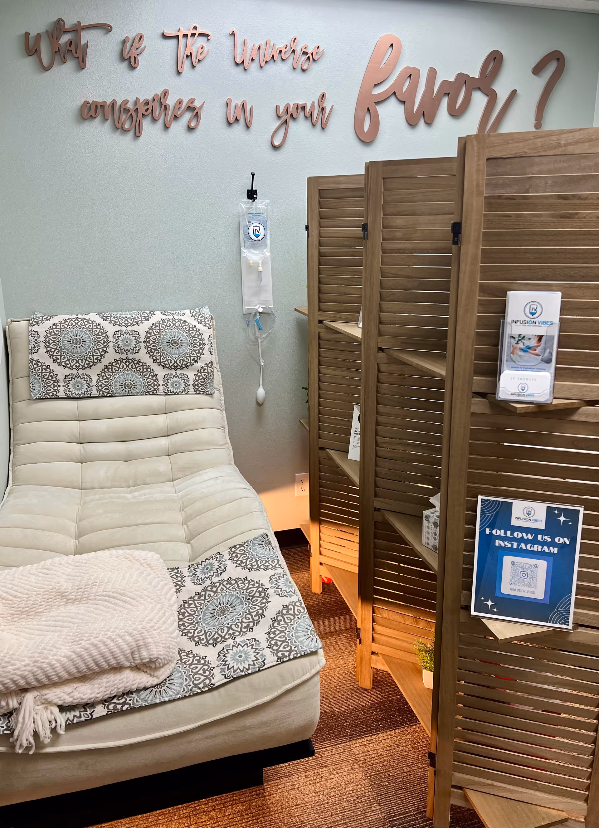 Infusion lounge with cream chaise, divider screens, wall art, and IV equipment.
