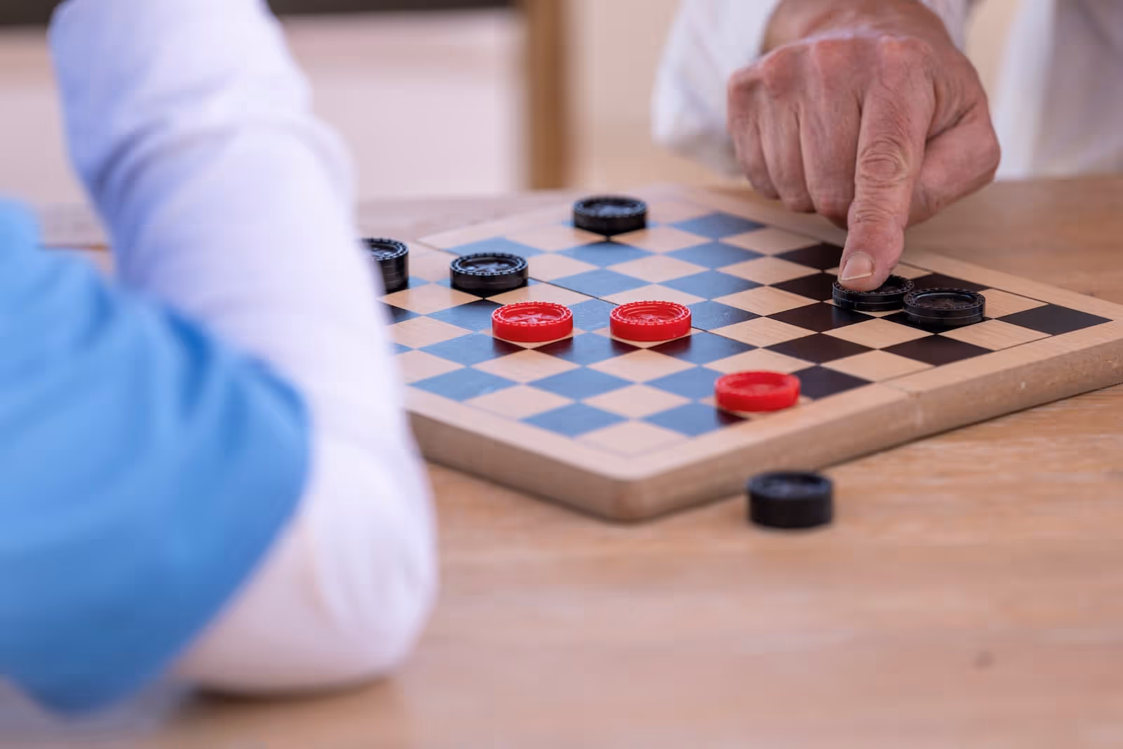 Close-up of elderly hands moving red and black checkers on a wooden board.