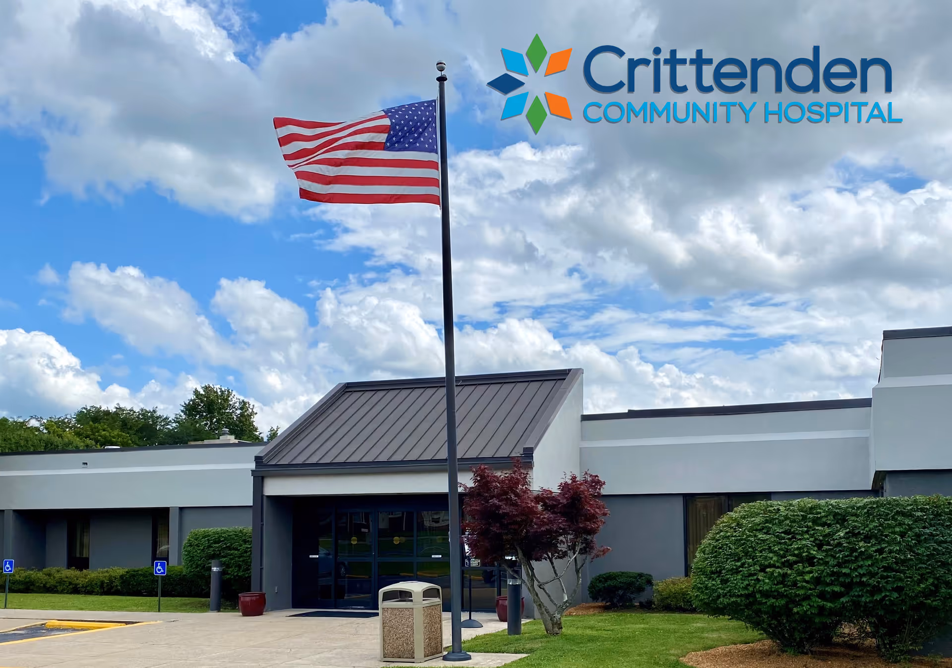 Exterior view of Crittenden Community Hospital entrance with flagpole, landscaping, and blue sky.