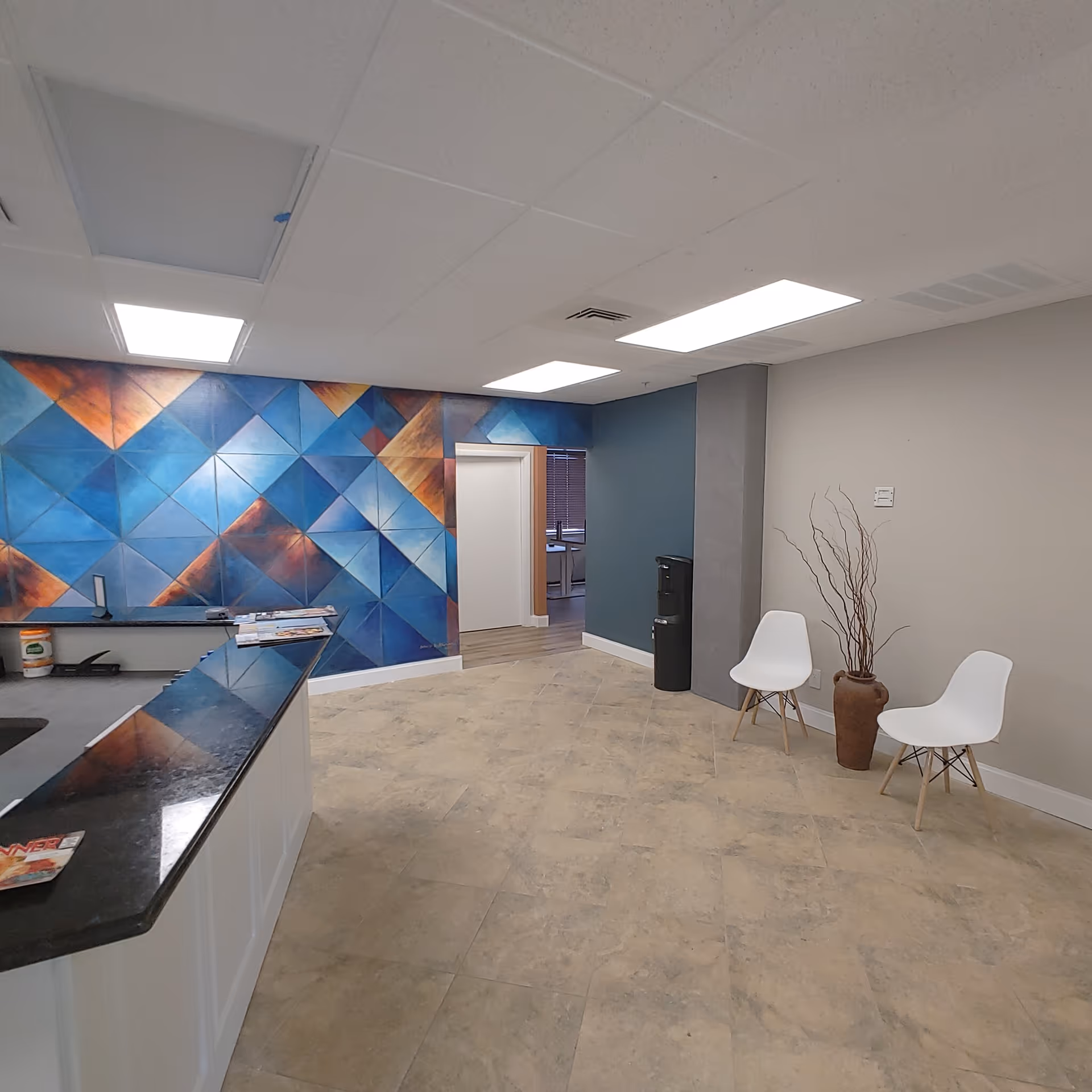 Lobby area with colorful geometric mural, reception counter, two white chairs, and a decorative vase.