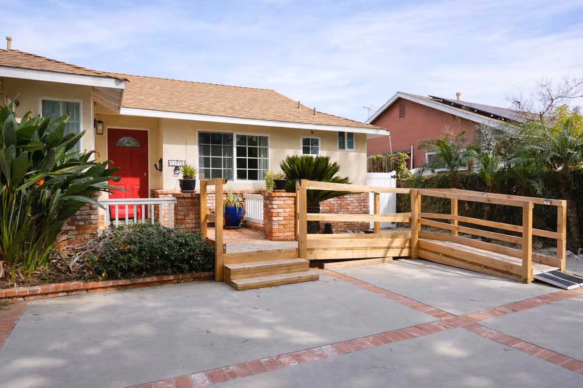 Front exterior of a single-story residence with wooden ramp, planters, and red door.