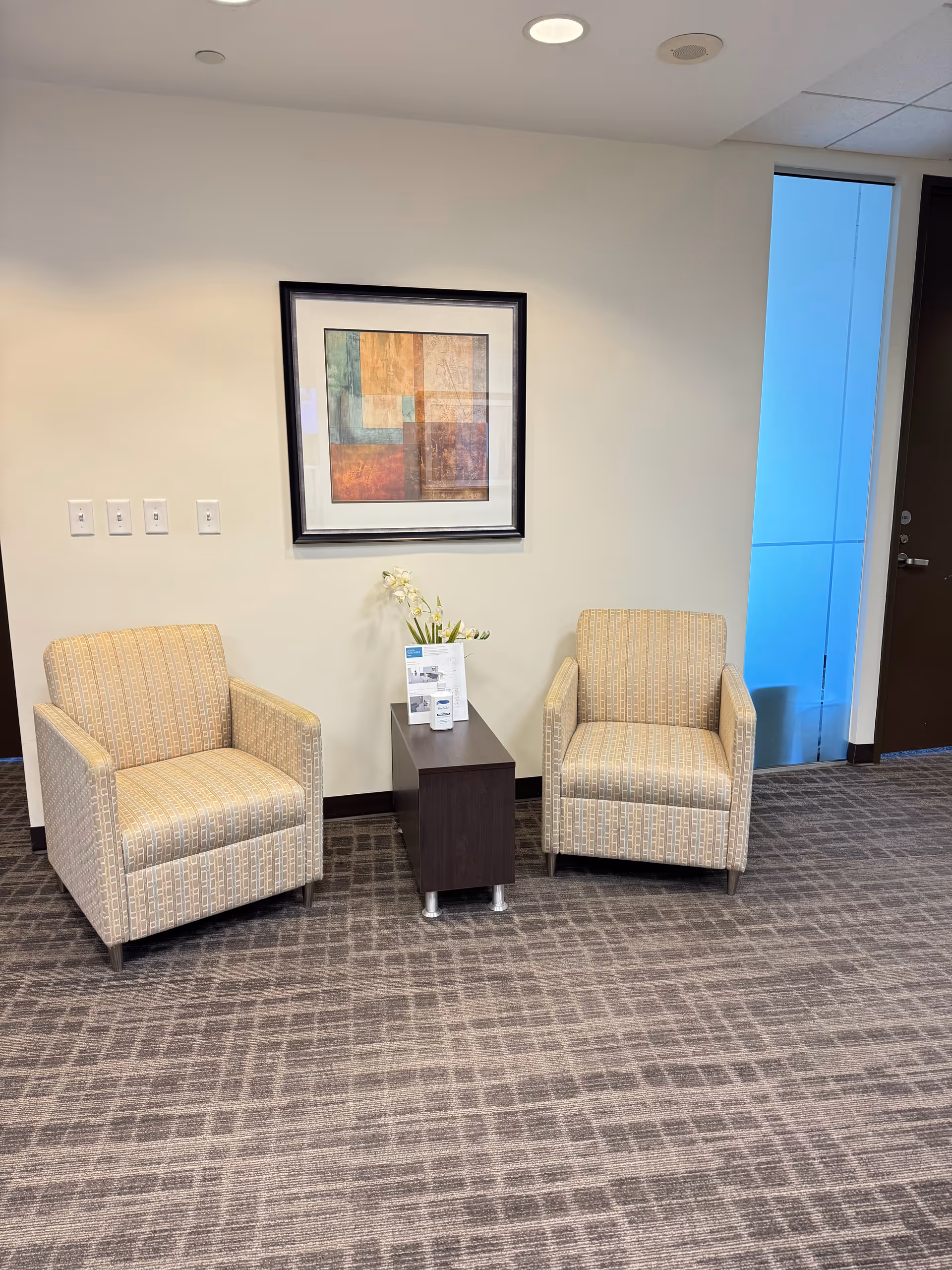 Two beige patterned chairs flank a small dark table in a neutral reception area.