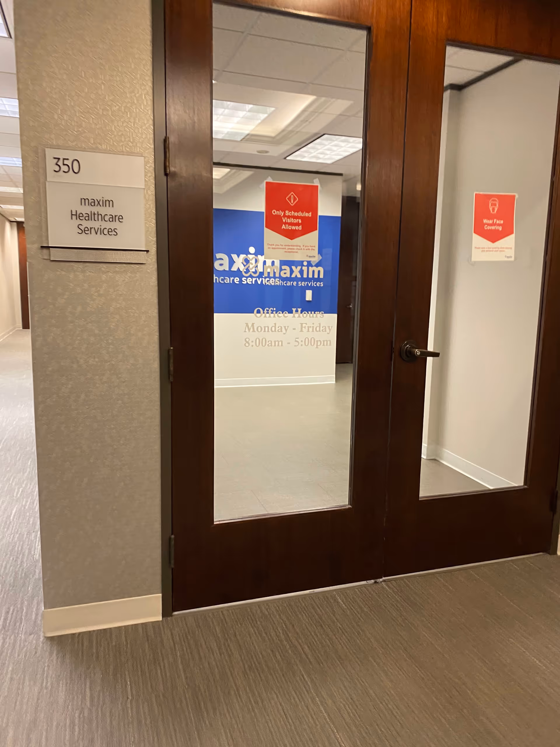 Wood-framed glass doors open to a Maxim Healthcare office hallway with signs.