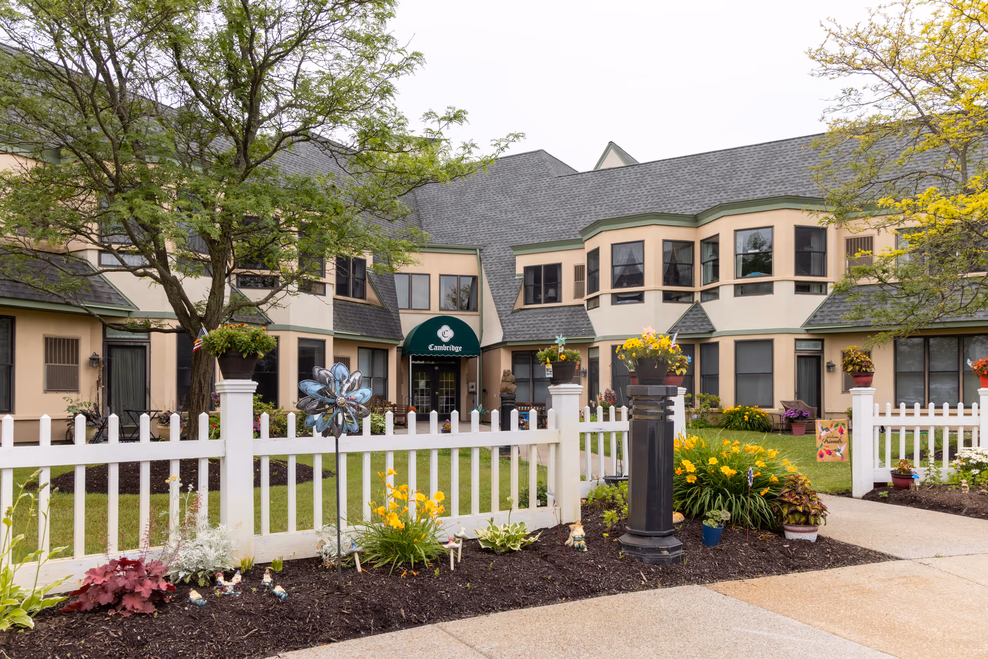 Senior living facility Canterbury Woods exterior with white fence, garden, and walkway.