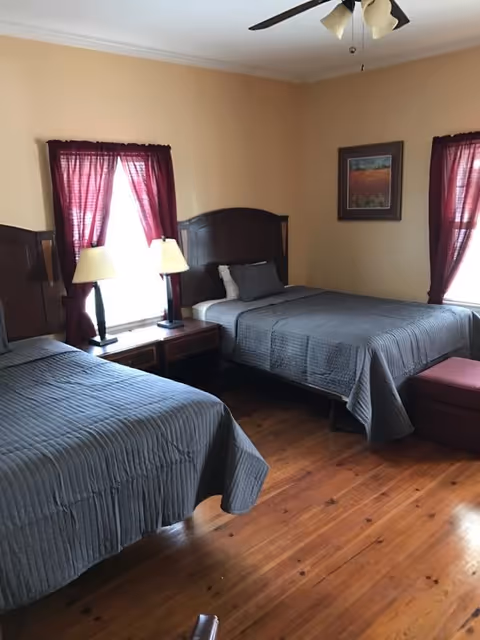 Two double beds in a cozy senior living room with matching furniture and burgundy curtains.