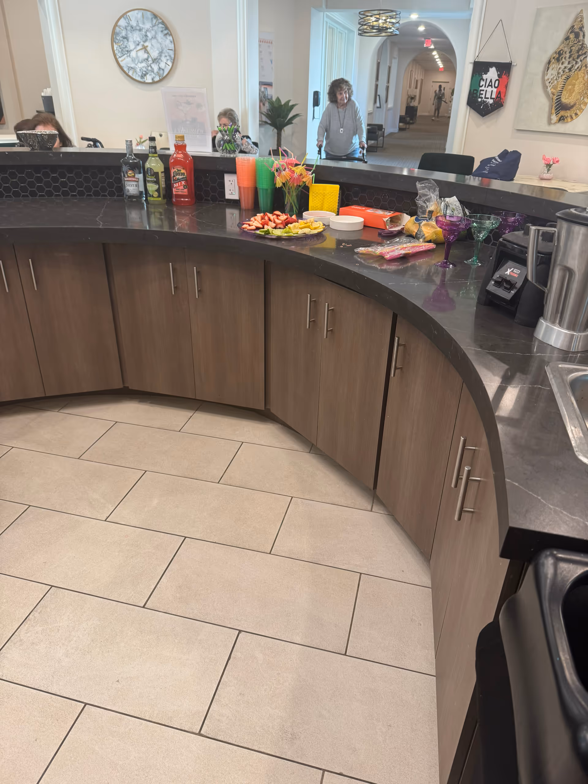Curved counter with drinks and snacks; staff and residents visible in the background.