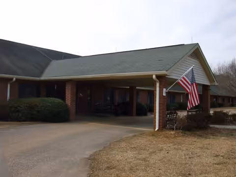 Front exterior of Sanford Manor Memory Care showing brick pillars and an American flag.