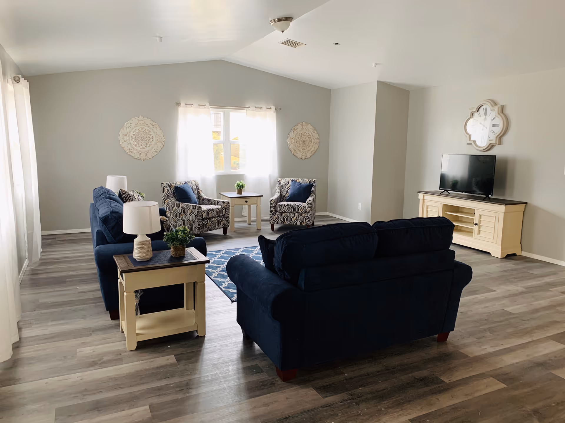Hartford Estates living room with blue seating, coffee tables, windows, and a TV.