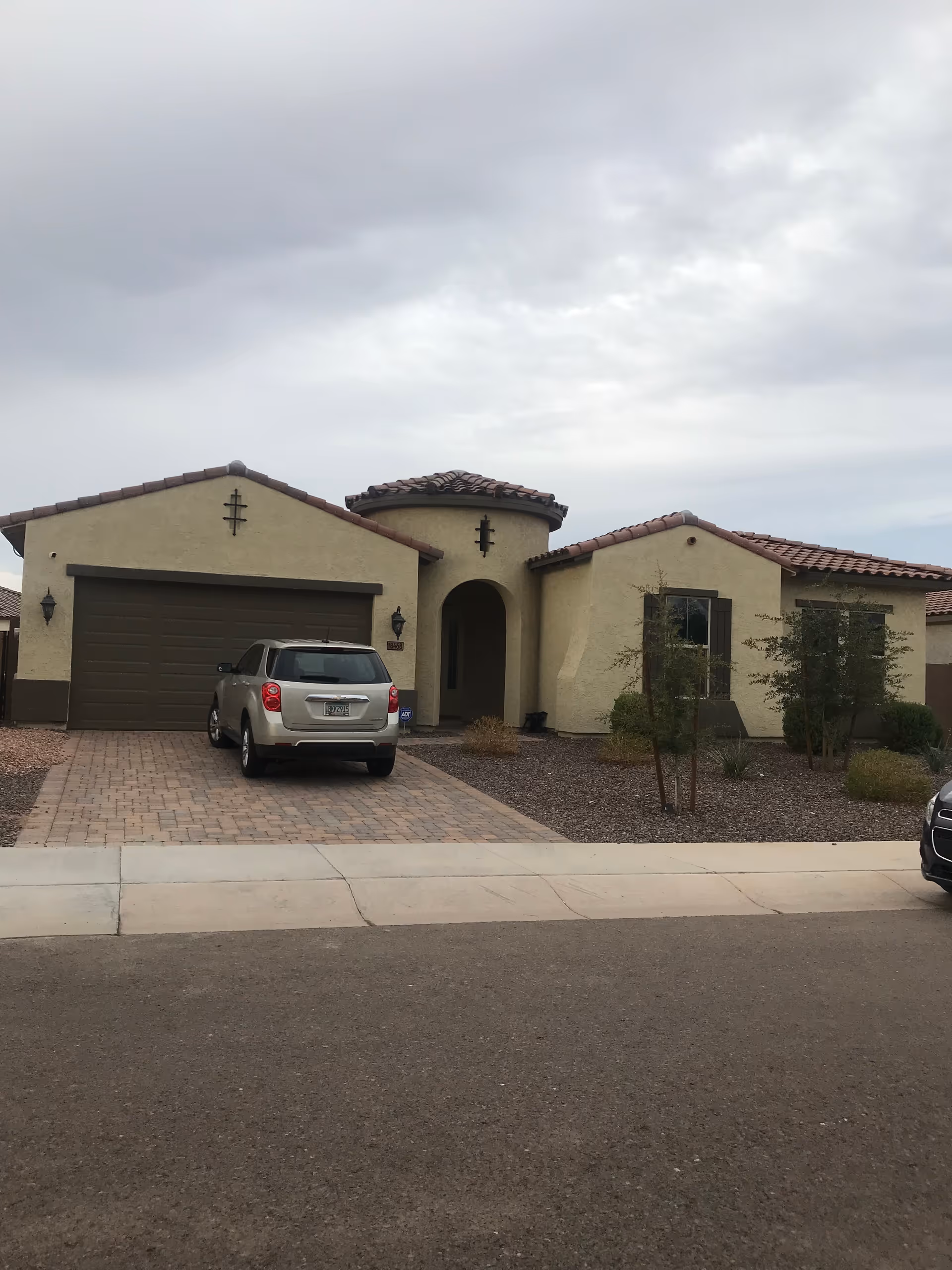 Front view of a beige southwestern-style home with driveway and parked car.