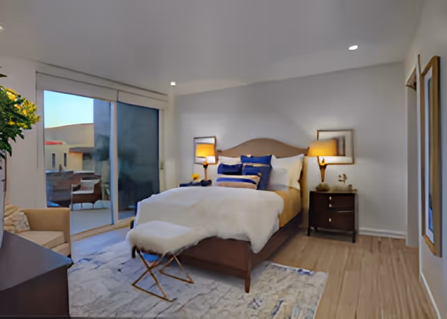 Contemporary bedroom with a made bed, bedside tables and lamps, a bench at the foot of the bed, and sliding glass doors leading to an outdoor patio.