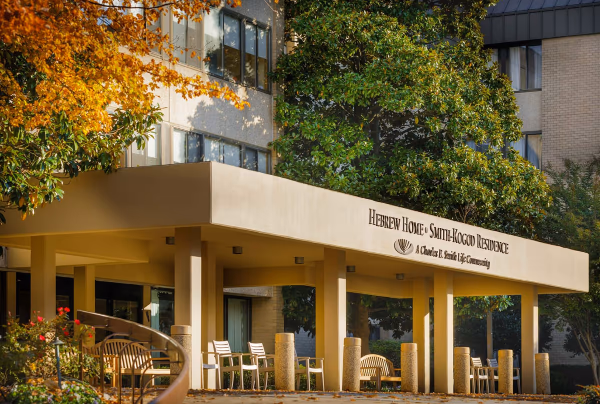 The entrance canopy of the Hebrew Home Smith-Kogod Residence with chairs and autumn foliage.