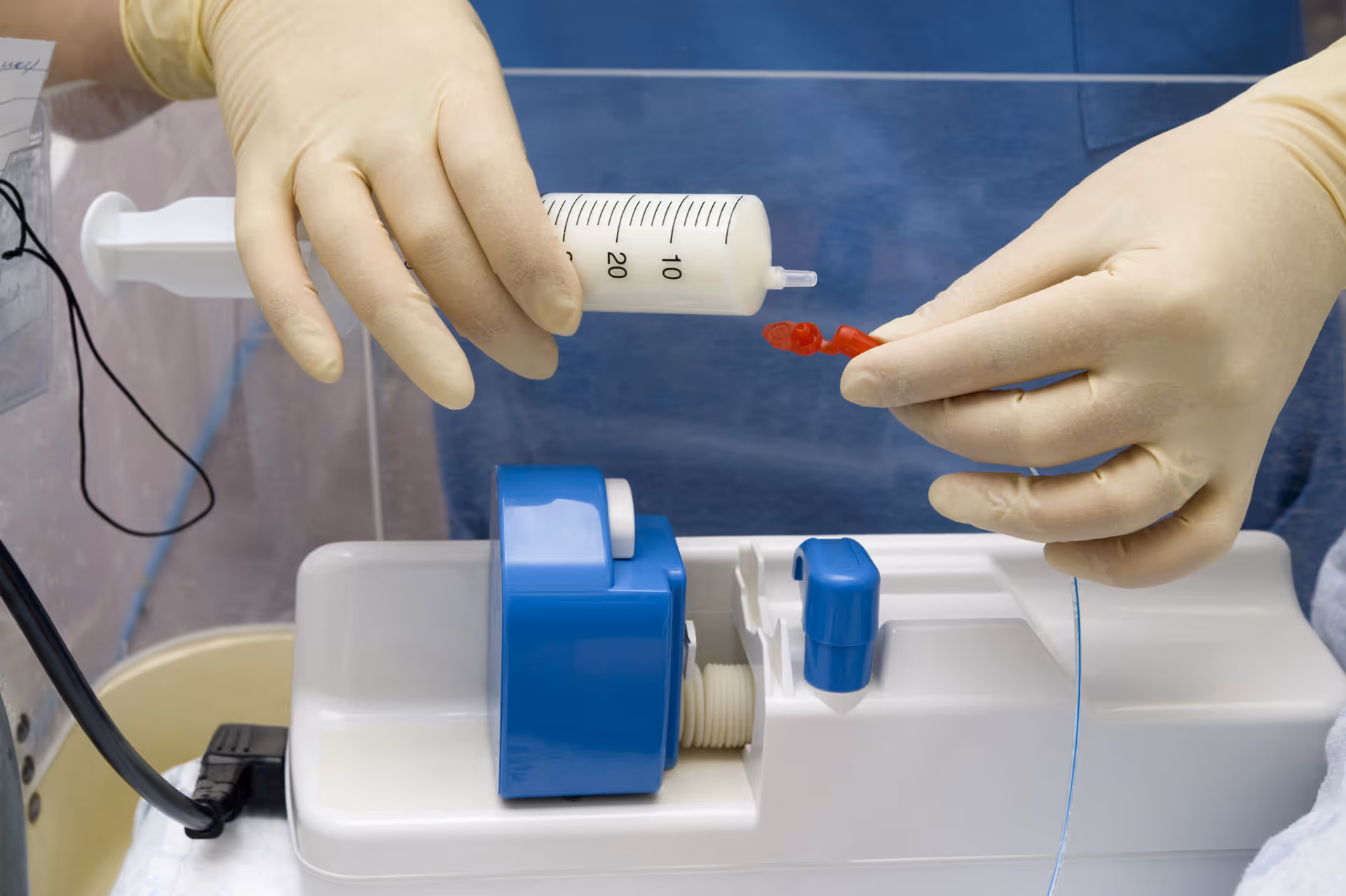 Close-up of gloved hands filling a syringe at a medical device in a clinical setup.