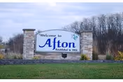 Outdoor stone sign reading 'Welcome to Afton' with 'Established in 1954' and landscaping.