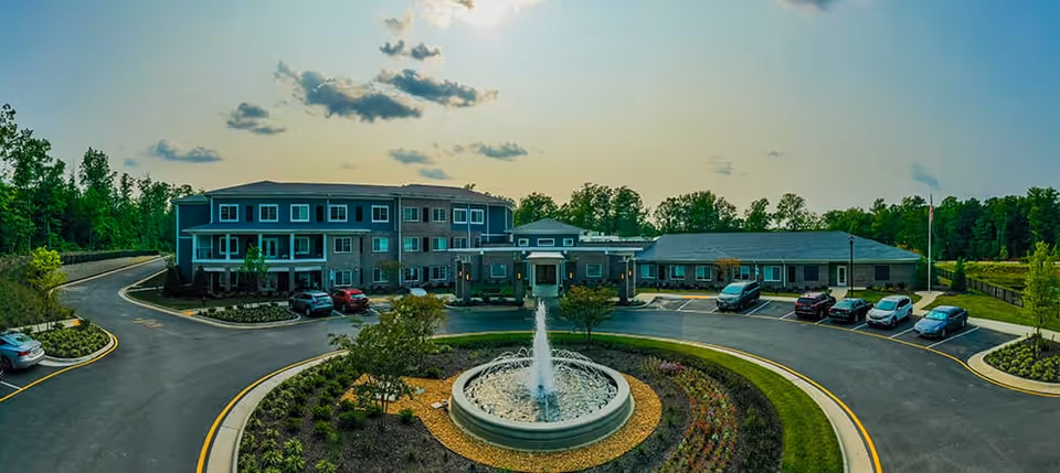 Front exterior of the Watercrest Richmond senior living building with a circular driveway, central fountain, landscaped beds and parked cars.