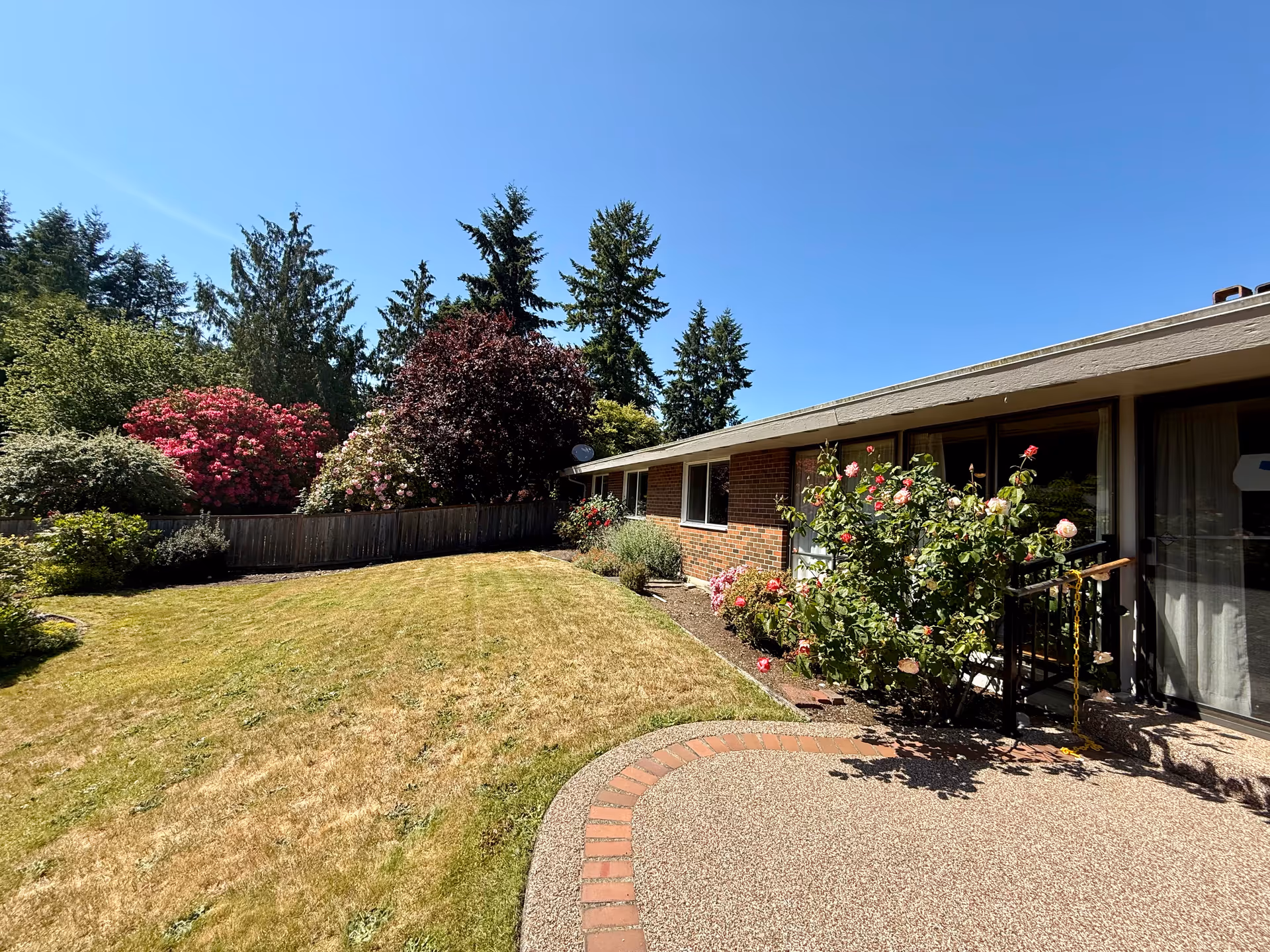 Brick single-story residence with manicured yard, flowering shrubs, and a curved patio by sliding doors.