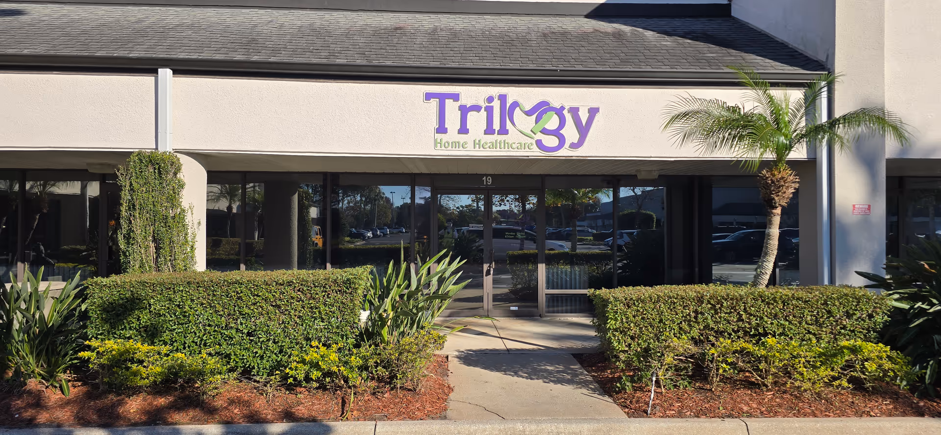 Front view of Trilogy Home Healthcare facility with glass entrance and manicured landscaping.
