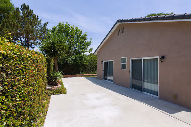 Outdoor concrete patio beside a beige senior living facility with sliding doors and green hedges.