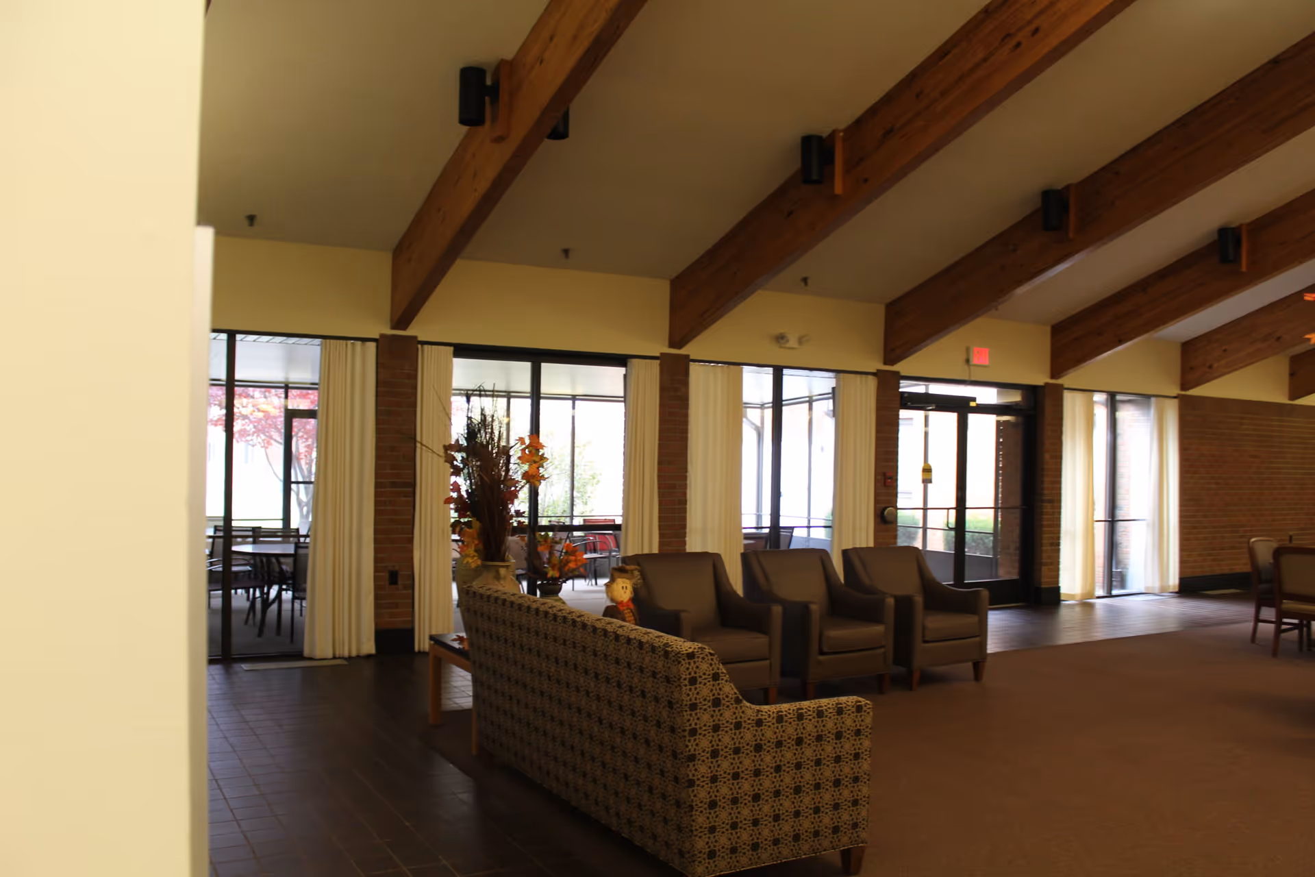 Interior senior living lobby with brown chairs, patterned sofa, brick columns, and wooden ceiling beams.