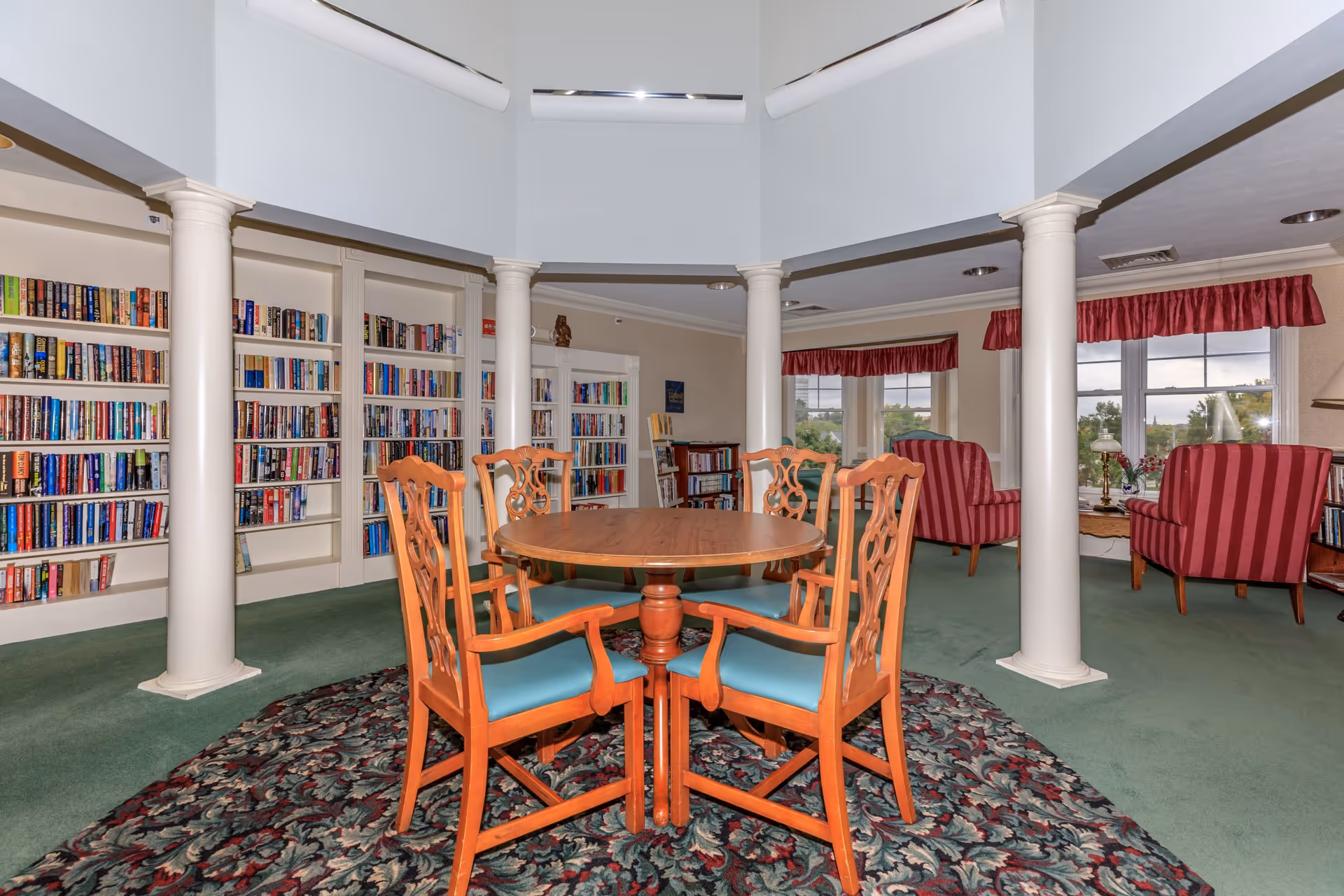 Circular wooden table with carved chairs and blue cushions in a library-style lounge.