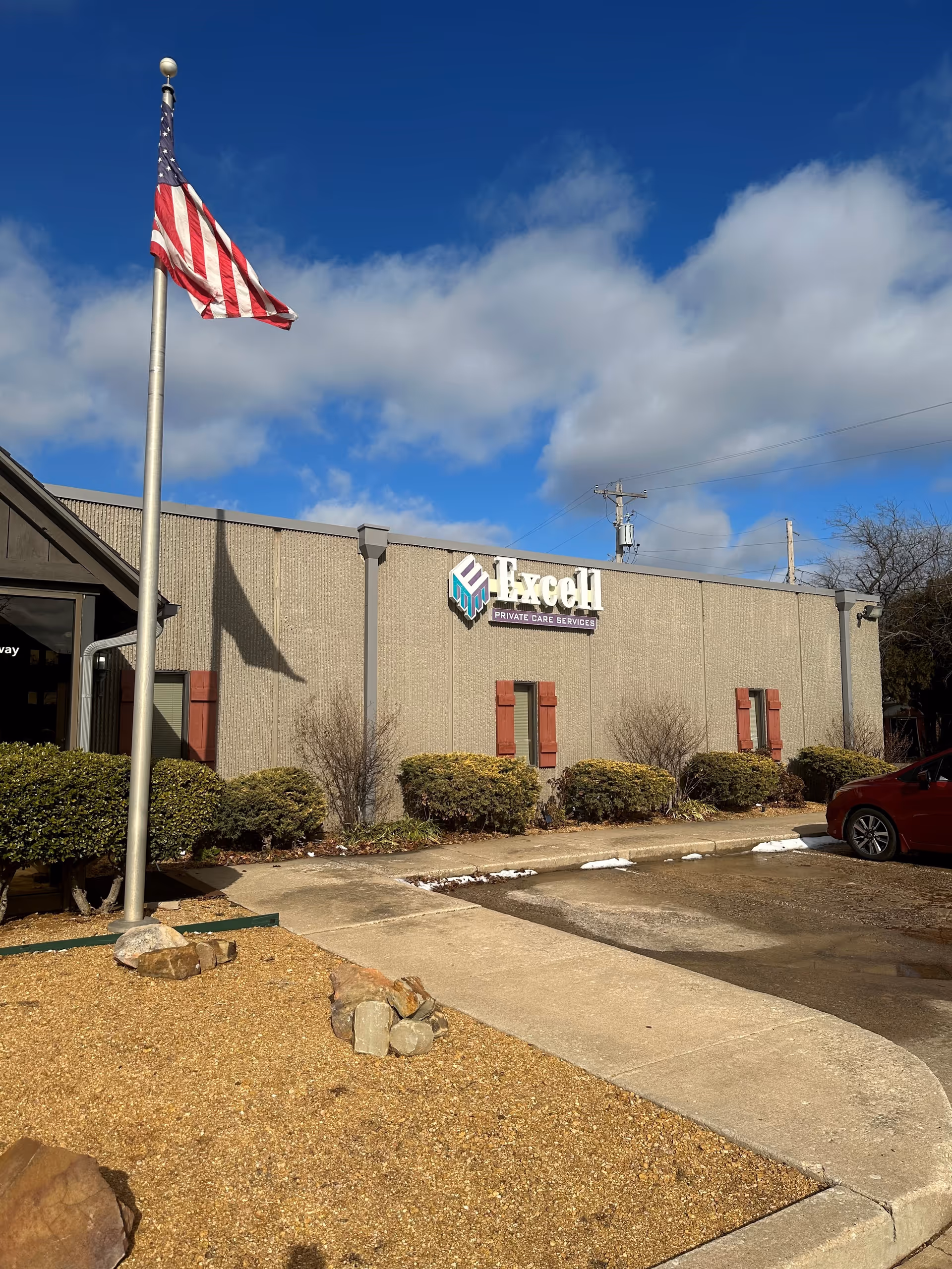 Exterior view of Excell Private Care Services building with American flag and blue sky.