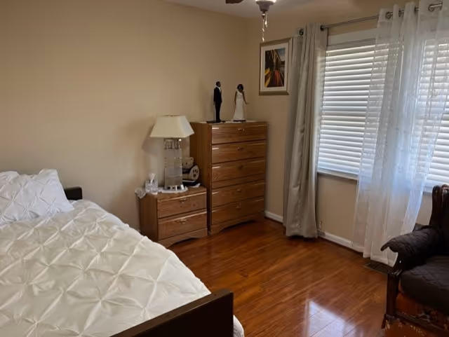 Bedroom with bed, dresser, lamp, and a window with sheer curtains.