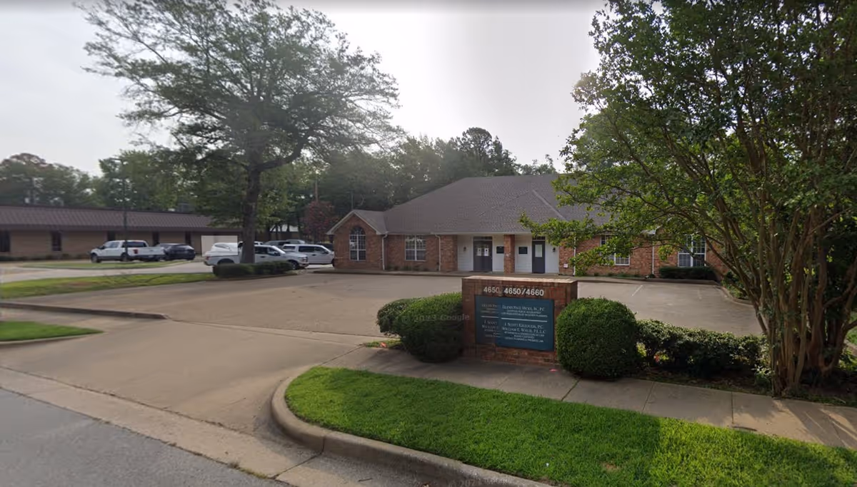 Exterior view of a brick senior living facility with a parking lot, entrance, and sign.