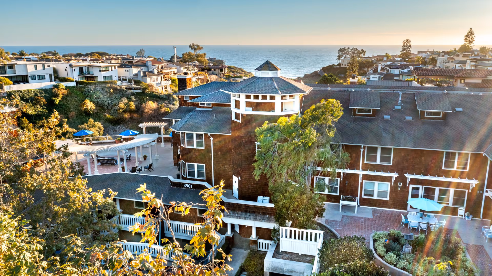 Aerial view of Crown Cove senior living facility with ocean backdrop and outdoor dining area.