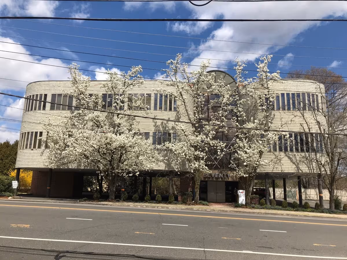 Exterior view of a three story building with curved windows and blooming trees.