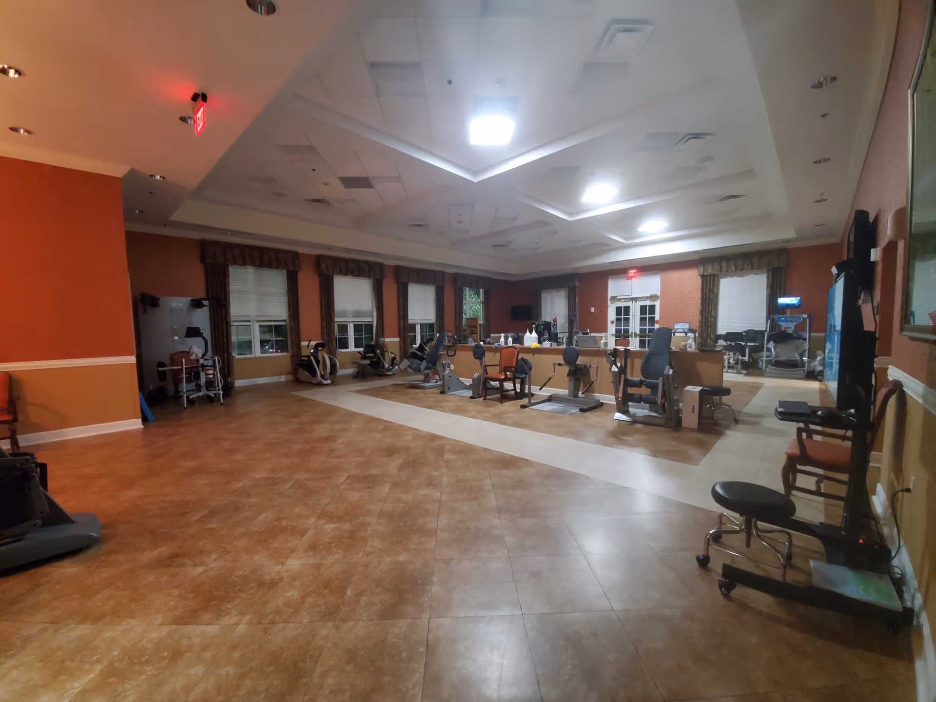 Spacious rehab gym with cardio machines and a reception desk in a warm interior.