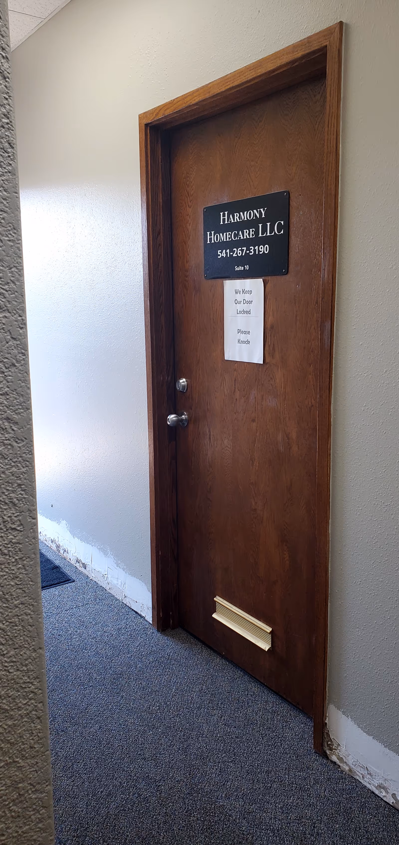 A wooden interior door with Harmony Homecare LLC sign in a hallway.