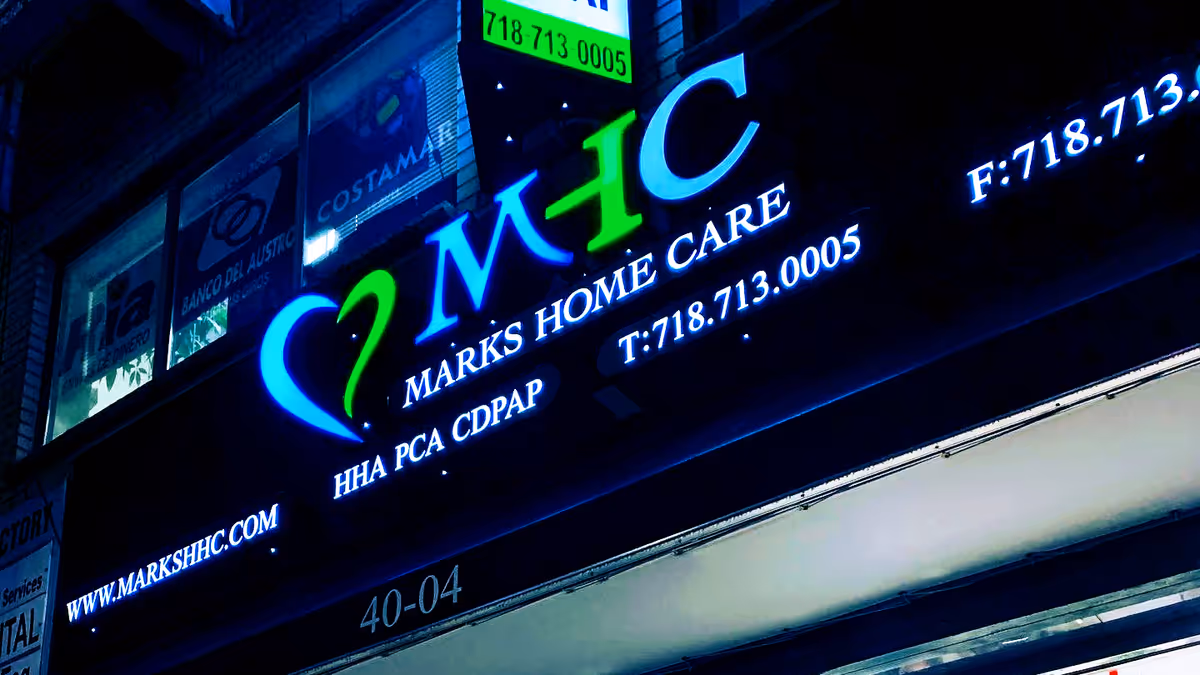 Nighttime storefront with neon MARKS HOME CARE sign on the building front.