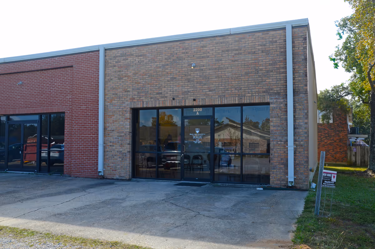 Brick commercial building with large glass doors and adjacent parking area.